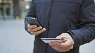 Akıllı telefon kullanan ve şehirde kredi kartı tutan genç adam, şehir ödemesi ya da alışveriş senaryosunu öneriyor..