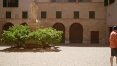 İspanya, Mallorca 'da odağını kaybetmiş bir adam ön planda bir heykel ve yeşillik ile duruyor ve bir bokeh etkisi yaratıyor..