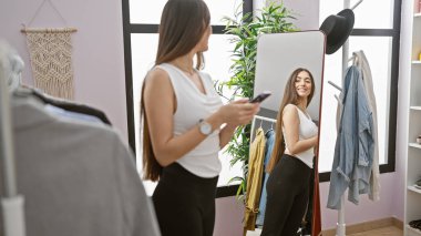 Soyunma odasında aynalı ve elbise askısı olan akıllı telefon kullanan bir kadın.