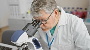 Mature man scientist using microscope in laboratory clipart