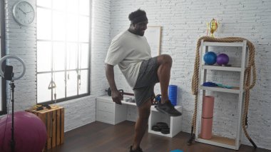 Genç Afro-Amerikalı bir adam spor salonunda egzersiz yapıyor. Spor malzemeleriyle etrafı geziyor..