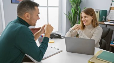 Man and woman coworking in a modern office with laptop, plants, and stationery, reflecting teamwork and partnership. clipart