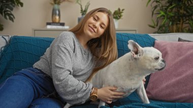 Sarışın, güzel bir kadın kanepede evcil köpeğiyle birlikte oturma odasında dinleniyor..