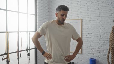 Spor salonundaki yakışıklı İspanyol genç adam arka planda spor ekipmanları olan kapalı bir spor merkezinde antrenman yapmayı düşünüyor..