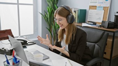 Modern ofis ortamındaki sanal bir toplantı sırasında kulaklıklı sarışın bir iş kadını..