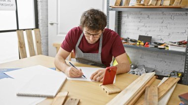 Odaklanmış bir zanaatkar, yaratıcı çalışma alanını çevreleyen aletler ve ahşap parçalarıyla iyi organize edilmiş bir marangozhanenin planını çizer..