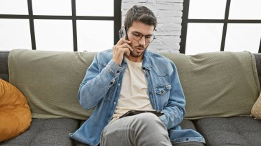 Sakallı İspanyol bir adam kanepede telefon kullanıyor, sıradan bir ev hayatı yaşıyor..