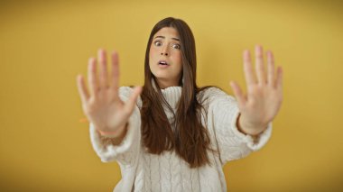 İzole edilmiş sarı bir arkaplan karşısında elleri havada, duygularını ifade eden, şaşırmış genç bir İspanyol kadın..