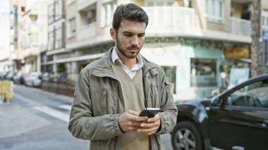 Meşgul şehir caddesinde akıllı telefon kullanan yakışıklı İspanyol..