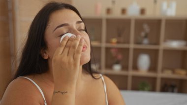 Sağlık merkezinde pamuklu bezle kaplıcada yüzünü temizleyen genç İspanyol kadın.