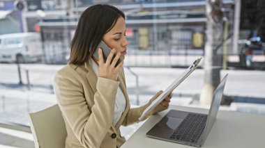 Modern bir ofiste çalışırken bilgisayar ve telefonla birden fazla iş yapan profesyonel bir İspanyol kadın..
