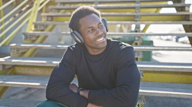 Gülümseyen Afro-Amerikan kulaklık takan adam güneşli bir günün tadını çıkarıyor..