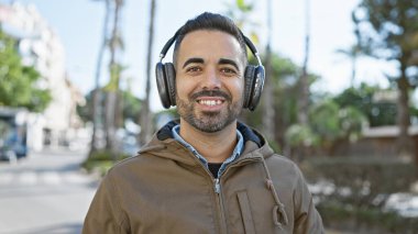 Şehir sokağında gülümseyen kulaklıklı yakışıklı İspanyol adam..