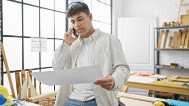 Genç bir adam telefonda konuşurken parlak bir marangozluk atölyesinin planını inceliyor..