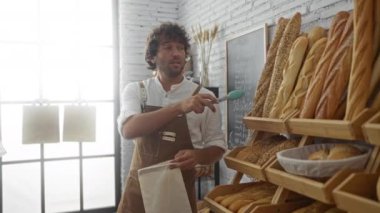 Pastanede ekmek sergisi ve kırsal iç mekan ile baget gösteren önlüklü genç bir adam.