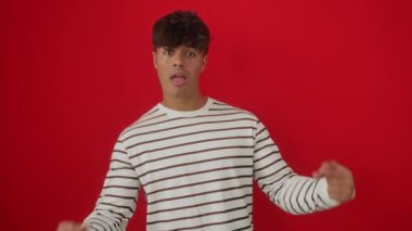 Kendine güvenen, çizgili tişört giyen, mutlu bir gülümsemeyle izole edilmiş kırmızı arka planda duran İspanyol bir adam.