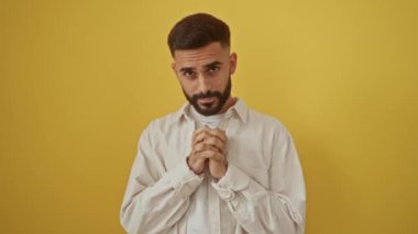 Sakallı genç adam sarı arka planda poz veriyor, ciddi ve neşeli ifadeler de dahil olmak üzere çeşitli duygular ve jestler sergiliyor.