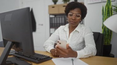 Ofiste yalnız kutlayan kıvırcık saçlı bir kadın telefonuna bakarken, orta yaşlı, Amerikalı, kapalı alanda çalışan.