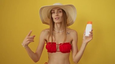 Bikinili kadın mutlu bir şekilde gülümsüyor ve gururla sarı arka planda güneş kremi sürüyor.