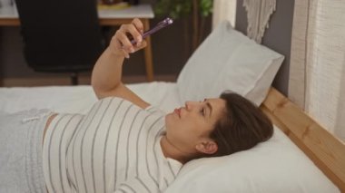 Genç bir kadın, oturma odasında günlük yaşamında duygularını gösterirken şaşırmış bir şekilde cep telefonu kullanıyor.