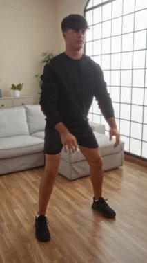 Modern bir apartman dairesinde spor kıyafetleriyle egzersiz yapan genç bir İspanyol.