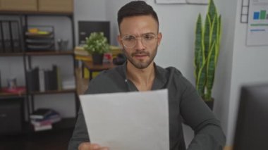 Ofis ortamında sakallı yakışıklı, genç, İspanyol bir adam. Odaklanmış bir ifadeyle belge okuyor..