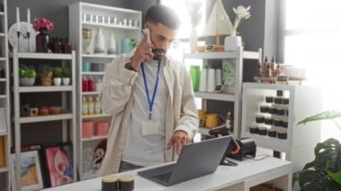 Ev dekorasyonu mağazasında sakallı genç bir adam dizüstü bilgisayar kullanırken etrafını çeşitli dekorasyon ve bitkilerle donatmış.