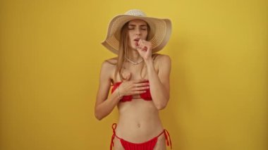 Bikini giyen ve yaz şapkalı bir kadın soğuk algınlığı ve bronşit yüzünden öksürüyor. İzole edilmiş sarı arka plan üzerine beyaz sağlık konsepti.