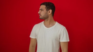 Beyaz tişörtlü, ciddi yüzlü, doğal ve sade görünen genç İspanyol bir adam izole edilmiş kırmızı arka planda kameraya bakıyor.