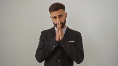 Sakallı, takım elbiseli genç İspanyol bir adam izole edilmiş beyaz bir arka planın önünde dua ediyor.