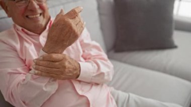 Oturma odasındaki kanepede otururken bileği ağrıyan yaşlı bir adam..