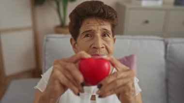 Oturma odasında otururken elinde kırmızı kalp şeklinde bir nesne tutan yaşlı bir kadın sıcak bir ev ortamında ilgi ve şefkat gösteriyor..