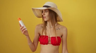 Bikinili kadın elinde güneş kremi tutuyordu. Şaşırmış, şaşırmış bir yüzü ve ağzı vardı. Sarı arka planda izole edilmiş, korkmuş ve inançsız görünüyordu.