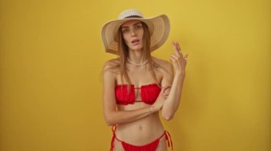 Kadın, beyaz, bikinili ve yaz şapkalı. Kafasına parmak doğrultulan bir silah yapıyor. İnzivaya çekilmiş sarı arka planda intihar jesti yapıyor.