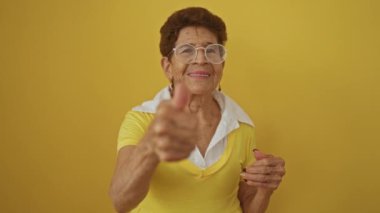Gözlüklü ve sarı tişörtlü yaşlı bir kadın izole edilmiş sarı bir arka plana gülümsüyor..