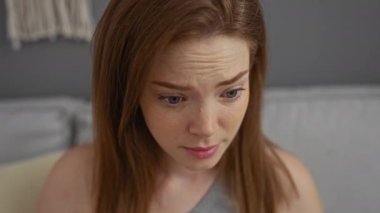 Evde alnındaki kırışıklıkları inceleyen genç bir kadın oturma odasında yüz ve ifadeye odaklanıyor.