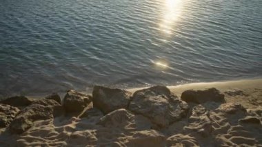 Sakin kayalık bir plajda gün batımı yumuşak dalgalarla kumlu sahilde, huzurlu bir sahil manzarası yaratıyor dinlenmek ve doğayı takdir etmek için mükemmel..