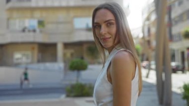 Çekici genç sarışın kadın güneşli bir günde arka planda binaları olan güvenli bir caddede duruyor..