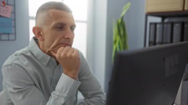 Motivasyon posterleri, organize çalışma alanı ve büyük pencerelerden gelen doğal ışık ile çevrili, parlak modern ofiste çalışan bir adam.