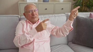 Oturma odasındaki gri bir kanepede gülümseyen yaşlı beyaz bir adam..