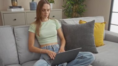 Genç bir kadın modern oturma odasındaki bir kanepede dizüstü bilgisayar kullanırken parmağını hiç kullanmıyor.