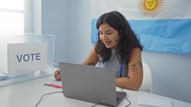 Arjantin bayrağı ve arka planda bir oy pankartı olan bir seçim üniversitesi odasında görüntülü konuşma yapan bir kadın.