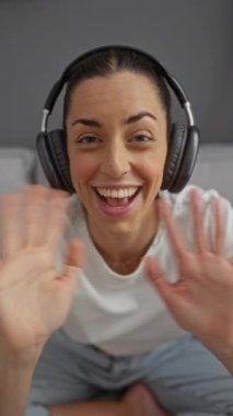Kulaklık takmış, gülümseyen ve şehirde bir sokakta mutlu mesut el sallayan bir kadın.