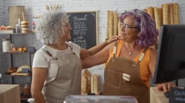 Olgun kadın fırıncılar sıcacık bir fırında gülümsüyor ve sarılıyorlar. Ekmek somunları ve hamur işleriyle sergileniyorlar. Sıcaklık ve ortaklık yayıyorlar.