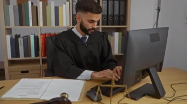 Yargıç cüppeli genç adam ofiste bilgisayarda çalışıyor kitaplar, tokmak ve teraziyle.