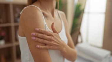 Zarif elleri olan bir kadın, sakin bir spa odasında omzuna dokunuyor. İçerideki güzellik ve sağlığın somut bir örneği..