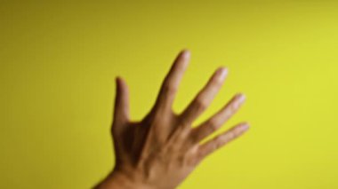 Bir adamın elini ve parmaklarını parlak sarı bir zemine yakın plan çekerek minimalist ve canlı tonlarda insan ayrıntılarına ve renk farklılıklarına dikkat çekiyor.