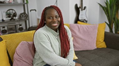 Modern bir apartman dairesinde örgü örüp gülümseyen Afrikalı Amerikalı kadın..