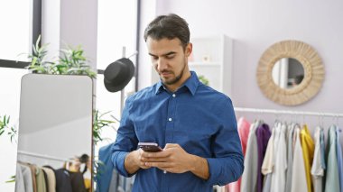 Yakışıklı İspanyol bir adam şık bir elbise odasında akıllı telefon kullanıyor. Aynası ve çeşitli kıyafetleri var..