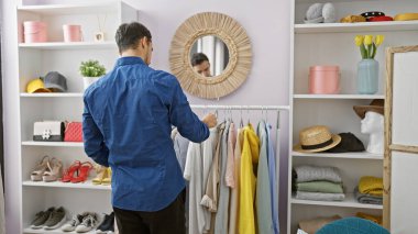 Mavi tişörtlü genç bir İspanyol iyi organize edilmiş bir odada aksesuarlarla dolu bir odaya göz atıyor..